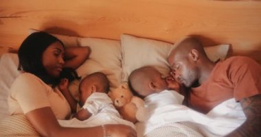 Küçük çocukları olan genç ebeveynler uyuyor ve yatakta kucaklaşıyorlar.