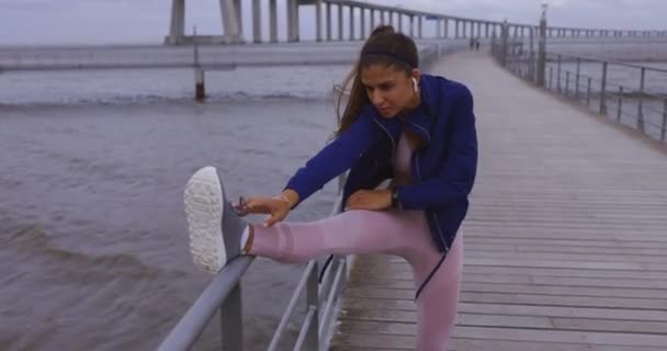 Mujer joven estirando la pierna después de correr por el puente del río — Vídeo de stock