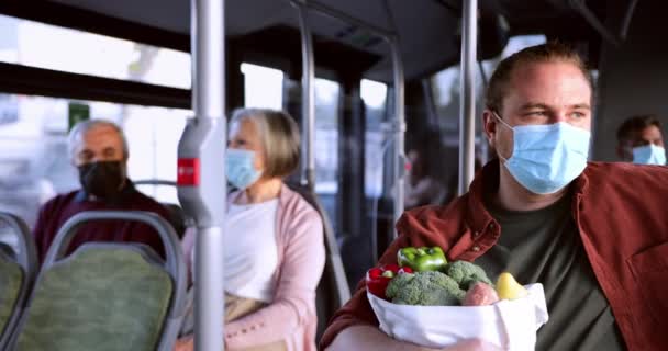 Hombre con máscara covid sentado dentro del autobús sosteniendo bolsa de compras — Vídeo de stock