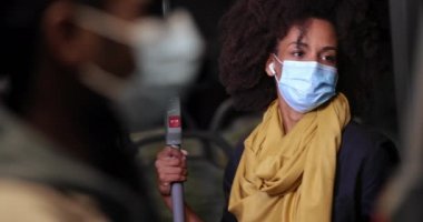 Otobüste akıllı telefonu, kulaklığı ve siyah maskesi olan Afro-Amerikalı bir kadın.