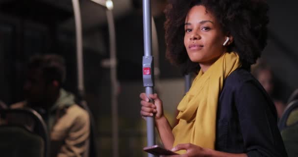 Afroamerikanerin mit Kopfhörer und Smartphone-Haltestange im Bus — Stockvideo