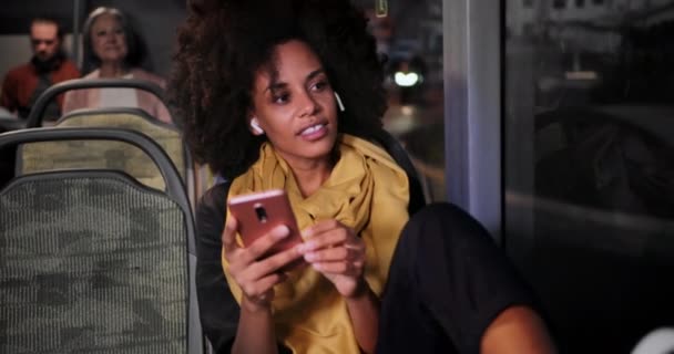 バスに座っているイヤホンやスマートフォンを持つクローズアップアフリカ系アメリカ人女性 — ストック動画