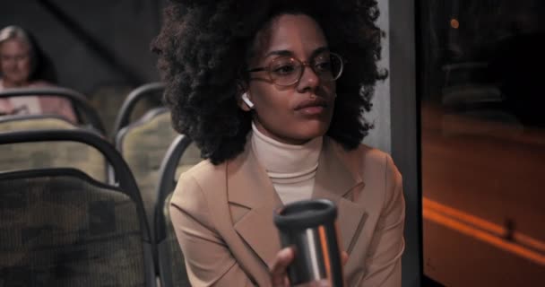 Afroamerykanka biznes kobieta ze słuchawkami trzyma kubek podróży w autobusie — Wideo stockowe