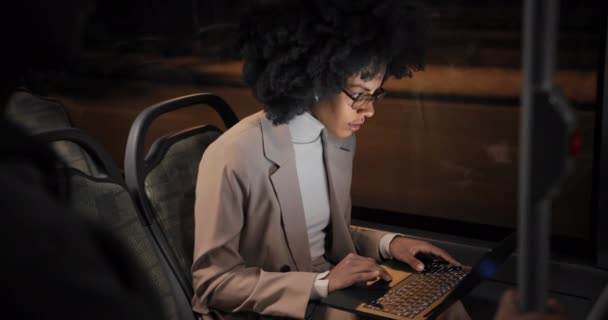 アフリカ系アメリカ人のビジネス女性がバスにイヤホンを装着したラップトップで働いています — ストック動画