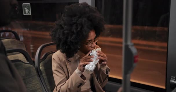 Африканско-американская деловая женщина ест нездоровую пищу в общественном автобусе — стоковое видео