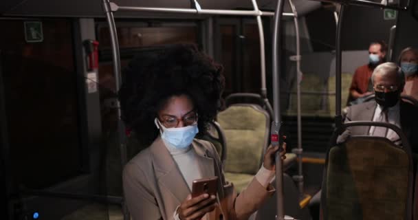 Afroamerikanische Geschäftsfrau mit greller Maske hält Smartphone im Bus — Stockvideo