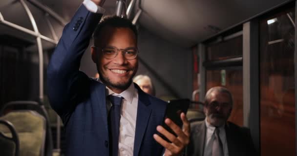 Uomo d'affari afro-americano sorridente che tiene smartphone su autobus pubblico — Video Stock