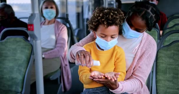 Afroamerykanka matka z covid maska dezynfekująca chłopiec ręce wewnątrz autobusu — Wideo stockowe