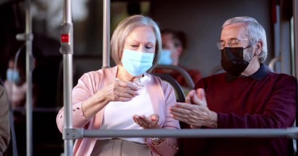 Starsza para w masce covid dezynfekującej ręce w autobusie — Wideo stockowe