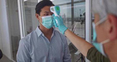 Ofiste çalışmadan önce maske takan bir adam sıcaklığı kontrol ediyor.