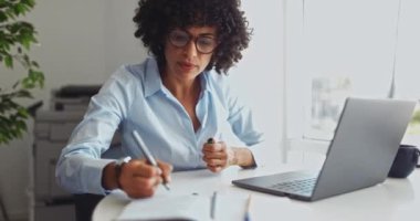 İş kadını ofiste dizüstü bilgisayarla notlar yazıyor ve çalışıyor.