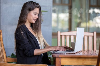 Modern terasta masa laptop üzerinde siyah ceketli kendine güvenen kadın yan görünüm