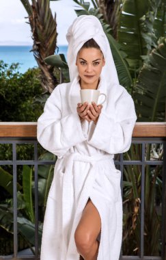 Bornoz terasta kahve fincan tropikal resort kameraya gülümseyen ile ayakta duş sonra genç ve güzel kadın