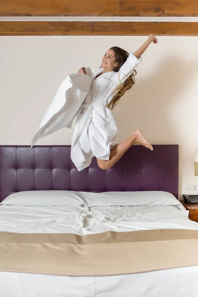 Güzel genç kadın bornoz el ile kadar yatakta otel odasında atlama