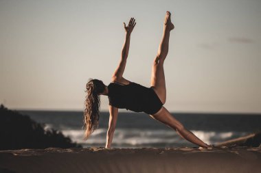 Arkadan Görünüş yan asana eğitim yoga yalnız kum plajındaki yaparken siyah elbise içinde ince kadın