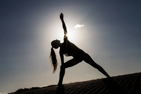 Silhouette of woman standing on beach and showing asana in sunlight