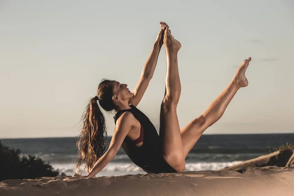 Siyah taytları kumlu plaj eğitim yoga güneş ışığı altında oturan kadın yan görünüm