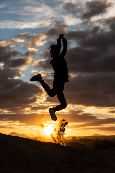 Silhouette of unrecognizable person jumping against wonderful cloudy sky in evening