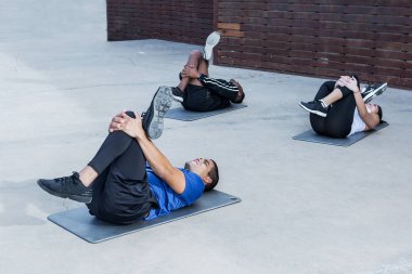 Mindere yalan ve bacak egzersiz çok ırklı erkek ve kadın için açık egzersiz sırasında gösteren yakışıklı spor eğitmeni