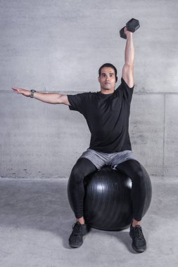 Konsantre kişisel antrenör siyah fitness topu üzerinde otururken omuz basın dumbbell ile yapıyor 