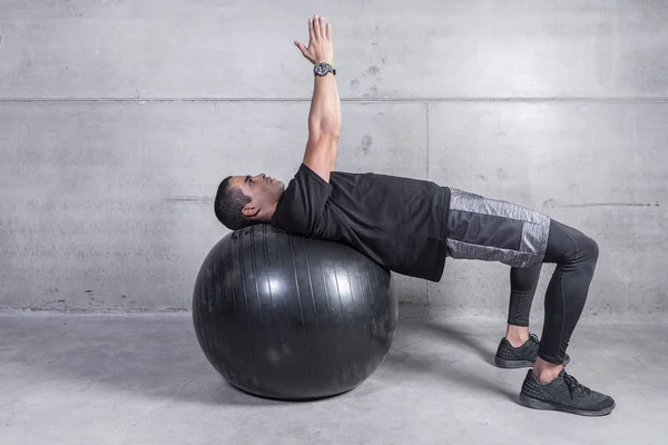 Professional trainer doing exercise while leaning on medicine ball and looking up with arms raised