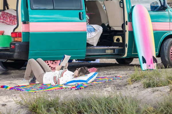 Woman lying on pillows near camping van and reading book in leisure, Lanzarote, Spain