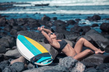 Kayalar sahil güneş ışığı zevk yakınındaki surfboard ile rahatlatıcı kadın güneş gözlüğü yatarken yan görünüm ıslak 