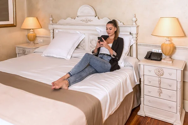 Joven bonita mujer usando teléfono inteligente en el dormitorio —  Fotos de Stock