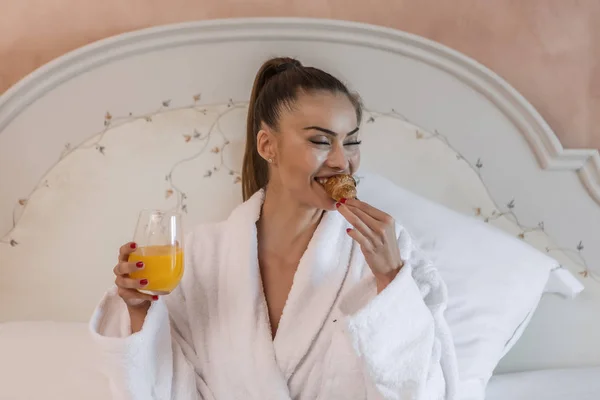 Lachende vrouw bijten croissant tijdens het ontbijt — Stockfoto