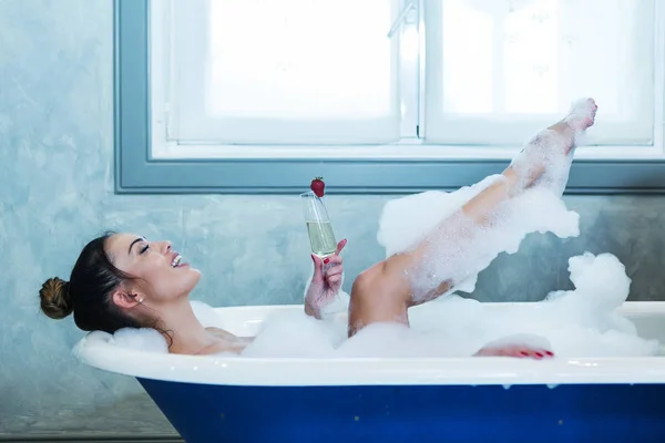 Cheerful female with champagne lying in bathtub