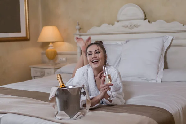 Веселая дама, наслаждающаяся алкоголем на кровати отеля — стоковое фото