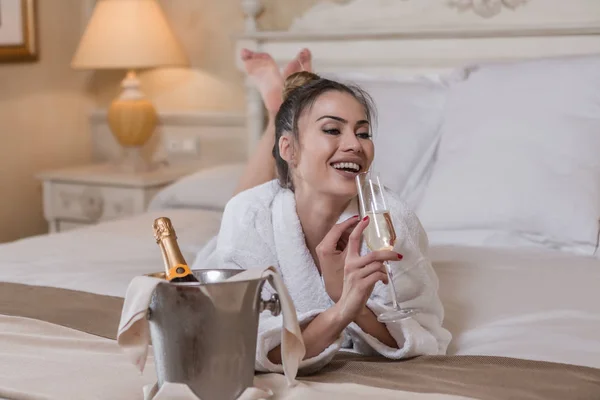 Donna ridente che beve champagne sul letto — Foto Stock