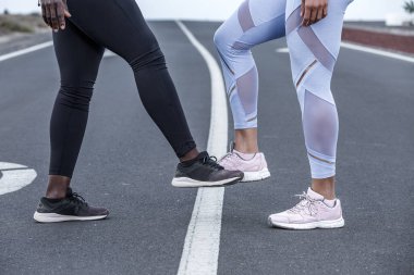 Tanımlanamayan çok ırklı kadın arkadaşlar asfalt yolda koşarken birbirlerini selamlıyorlar.