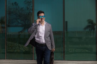 Erkek girişimcinin gülümseyip, cam binanın yanında yürürken akıllı telefon konuşması yapmasına sevindim.