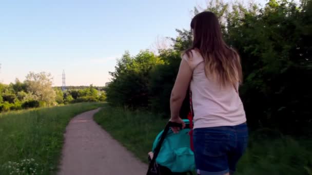 Moeder met een baby in een wandelwagen loopt in het park — Stockvideo