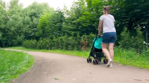 Moeder met een baby in een wandelwagen loopt in het park — Stockvideo