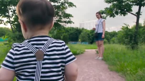 Petit enfant blond caucasien drôle apprend à marcher dans le parc, faire les premiers pas et tomber sans garder son équilibre sur la pelouse verte. — Video