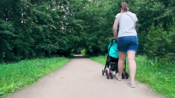 Mama z dzieckiem w wózku spacerowym po parku — Wideo stockowe