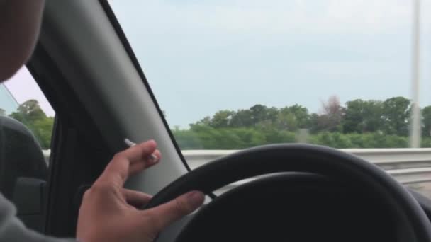 女性は車を運転しながらタバコを吸う。ハンドルに手を近づけて — ストック動画