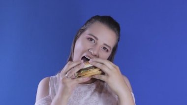 Orta boy. Seksi kız hamburgeri yalar ve kameraya gösterir.