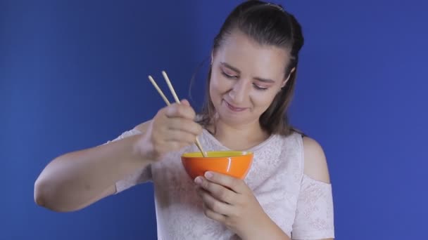 Giovane bella ragazza caucasica mangiare da una ciotola arancione con bacchette cinesi — Video Stock