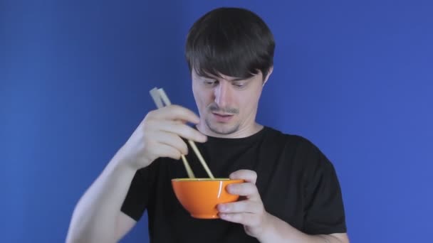 Fiatal jóképű fehér férfi eszik narancssárga tál kínai evőpálcikával — Stock videók