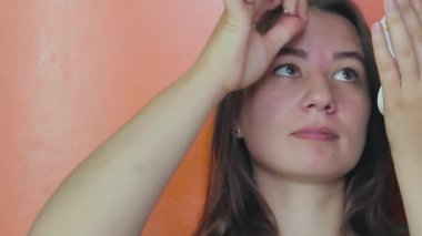 Kahverengi gözlü bir kız cımbızla kaşlarını yoluyor. Yakın plan.