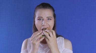 Açgözlülükle hamburger yiyen genç ve güzel bir kadın. Tam ağız.