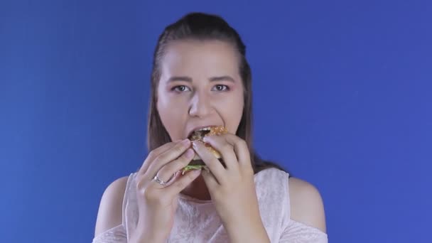 美しい若い空腹の女性が喜んでバーガーを食べる。口いっぱいに — ストック動画