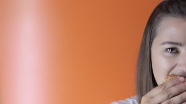 Turuncu arka planda hamburger yiyen bir kız. Boşluğu kopyala