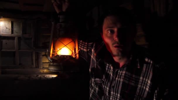 Joven hombre asustado en una casa vieja ilumina la pasarela con una lámpara de queroseno — Vídeo de stock