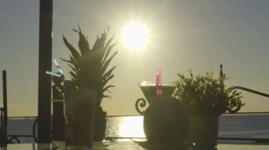 Arka planda güneş batan bir masada birden fazla kokteyl.