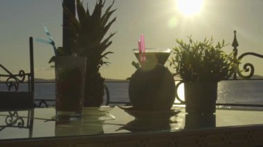 Arka planda güneşin denize battığı bir masada birden fazla kokteyl.