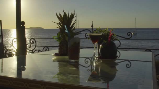 Flera drinkar på ett bord med solnedgång i havet i bakgrunden — Stockvideo